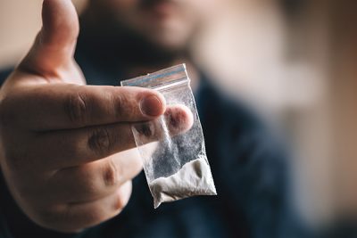 A bag of cocaine being held out by a teen cocaine user.